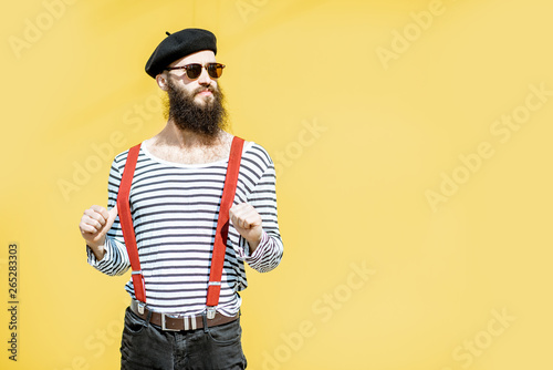 Portrait of a stylish bearded man dressed in striped shirt, suspenders and hat on the yellow background outdoors photo