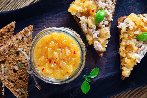a glass jar of pineapple and chili confiture covering chicken rillettes , sandwiches with the rillettes on black serving board