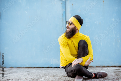 Portrait of a stylish man in yellow sweater sitting on the blue wall background outdoors © rh2010
