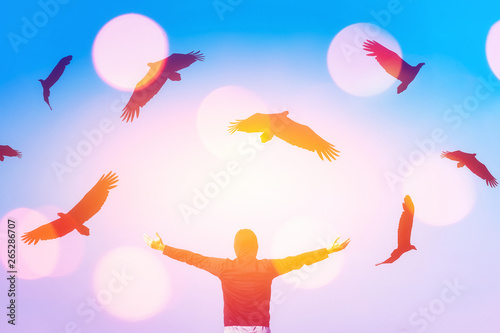 Man raise hands up on blue sky with eagle birds flying and colorful bokeh light abstract background.