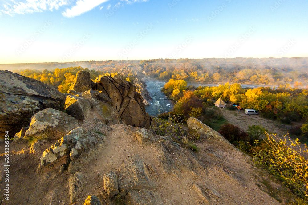 View from the cliffs on mountain river with yellow trees foliage and rocks on the shore at sunrise. Autumn landscape.