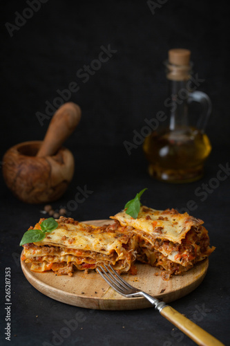 Traditional italian lasagna with vegetables, basil, minced beef meat, tomato and cheese on concrete background.