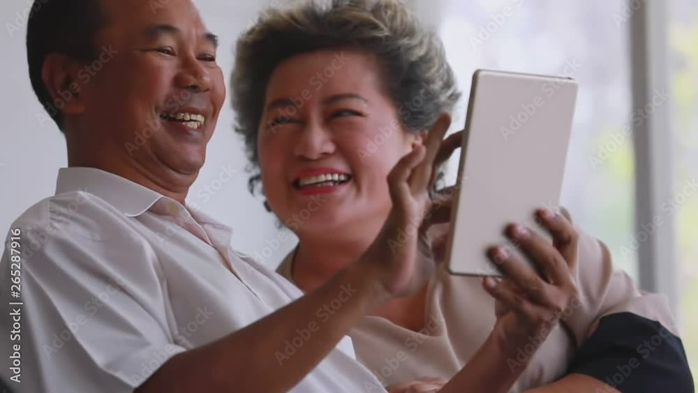 Slow motion scene video of senior Asian couple sitting on sofa and using tablet in living room, they smiling and laughing. Slow motion scene video of senior Asian couple sitting on sofa and using tablet in living room, they smiling and laughing.