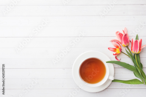 Cup of tea and flowers tulips on white table with copy space. Flat lay, top view.