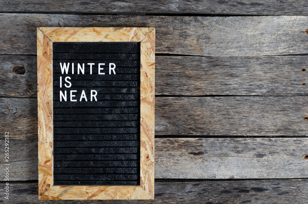 Letter board with white lettering winter is coming on old wooden background.