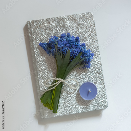 a notebook on a white background, silver cover, a bouquet of blue spring flowers, a blue candle photo