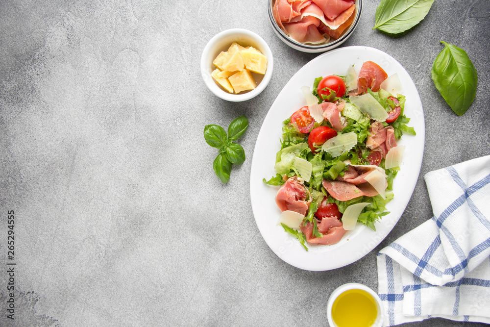 Salad with jamon (parma, ham, serrano, prosciutto), parmesan cheese, lettuce, cherry tomatoes on a plate. Delicious lunch, healthy food, Italian (spanish) cuisine Salad with jamon (parma, ham, serrano, prosciutto), parmesan cheese, lettuce, cherry tomatoes on a plate. Delicious lunch, healthy food, Italian (spanish) cuisine