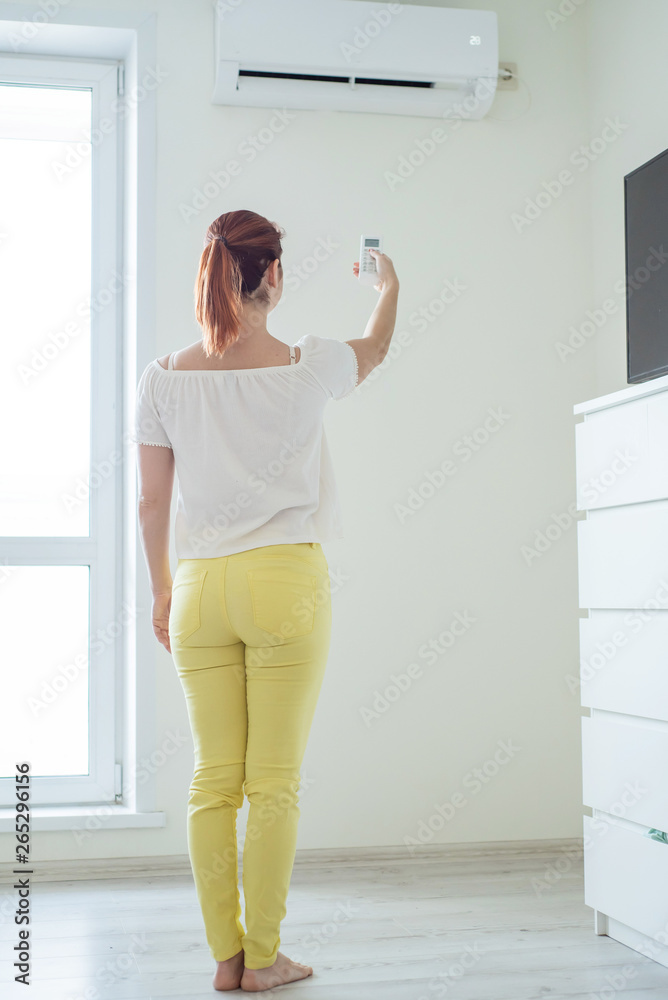 Red-haired woman stands back and holds a remote control air conditioner at home. Air conditioning in the apartment Red-haired woman stands back and holds a remote control air conditioner at home. Air conditioning in the apartment