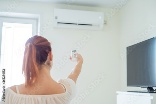 Red-haired woman s hand turning on the air conditioner. Red-haired woman stands back and holds a remote control air conditioner at home. Air conditioning in the apartment