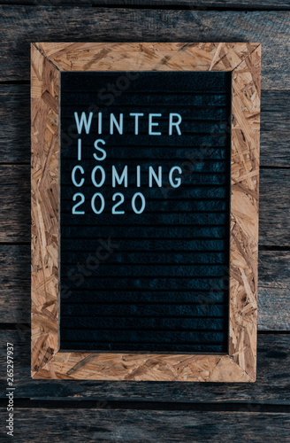 Letter board with white lettering winter is coming on old wooden background.