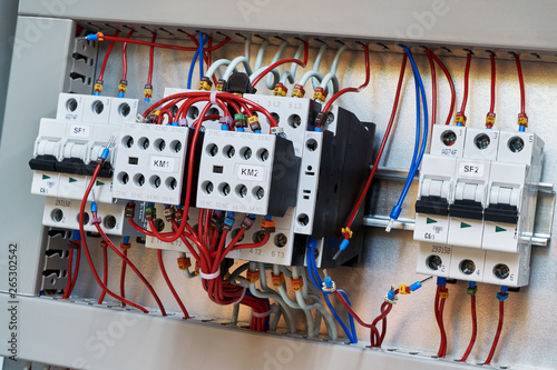 Two contactors with additional contacts and modular circuit breakers on the mounting panel in the electrical Cabinet. Electrical wires are connected to contactors, circuit breakers and contacts.