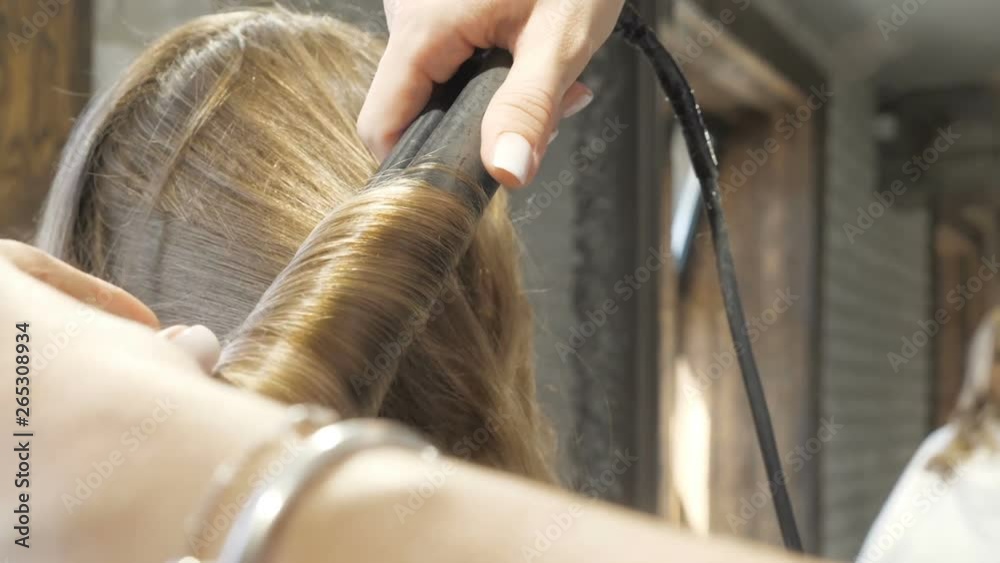 Hairdresser is straightening the client's hair in a beauty salon.