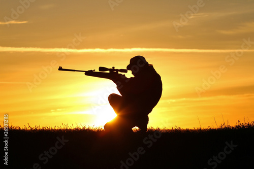 Silhouette of a man with a rifle on the background of a beautiful sunset, the boy shoots a gun