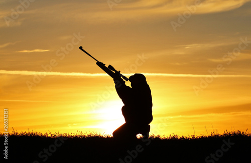 Silhouette of a man with a rifle on the background of a beautiful sunset  the boy shoots a gun