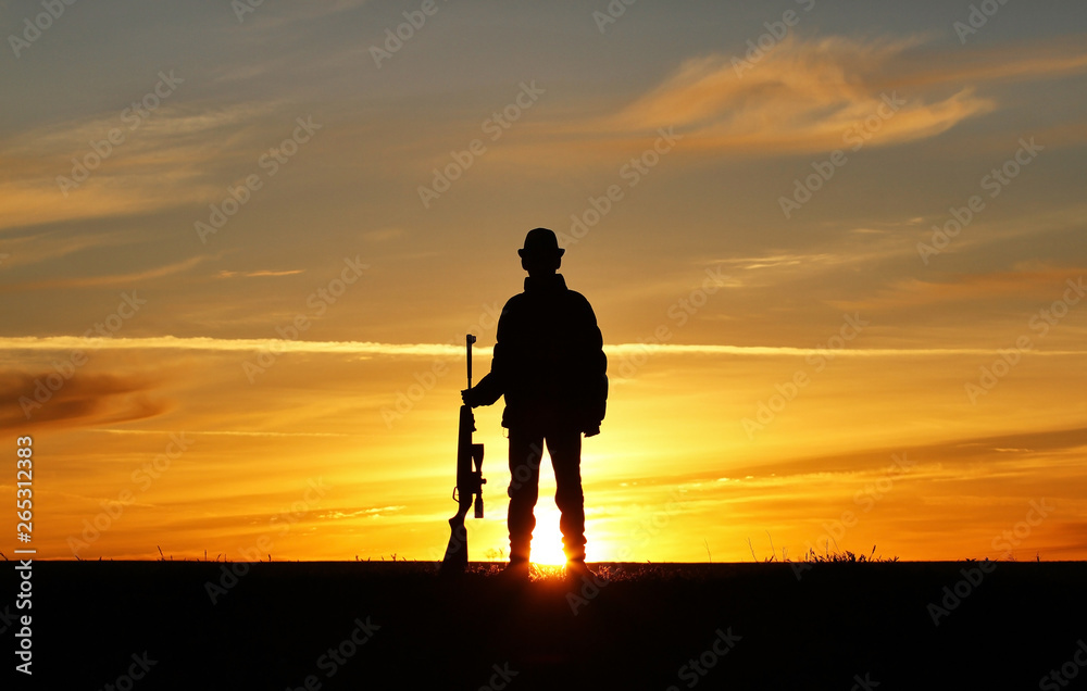 Silhouette of a man with a rifle on the background of a beautiful sunset, the boy shoots a gun