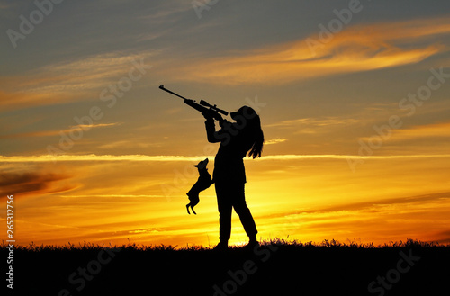 Silhouette of a girl with a rifle at sunset with a dog, a breed miniature pinscher