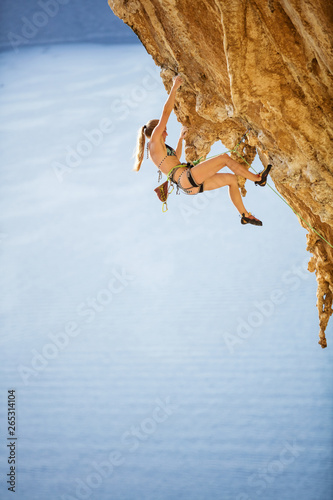 Young woman in bikini climbing challenging route on overhanging cliff