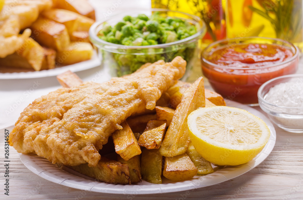 Traditional British street food fish and chips with ketchup sauce and mushy peas on paper plate