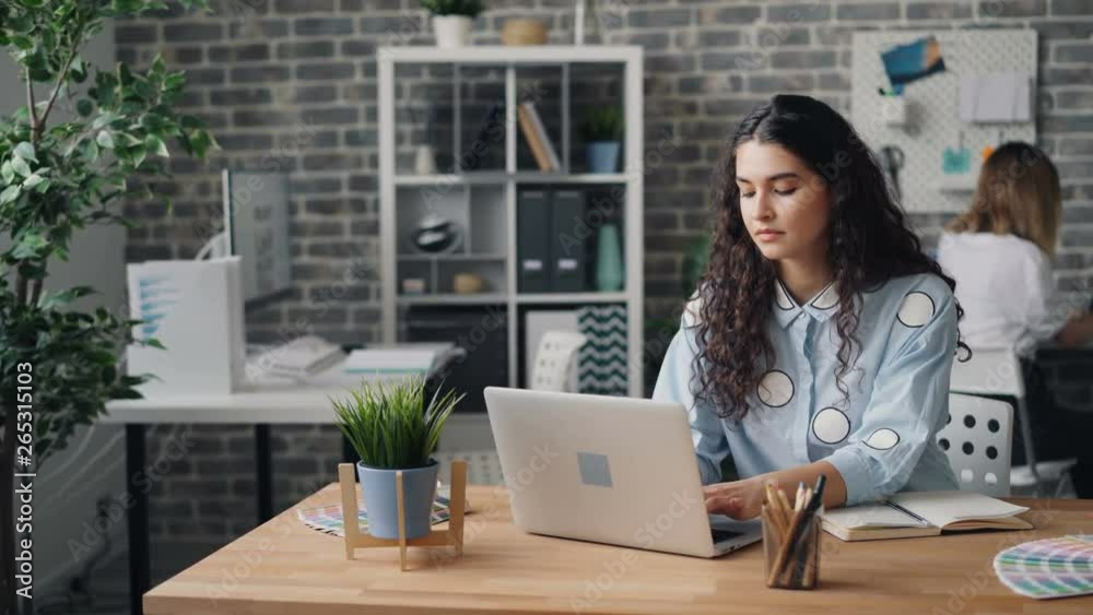 Young woman serious employee is working with laptop in office doing work in internet sitting at desk. Millennials, shared workspace and modern technology concept. Young woman serious employee is working with laptop in office doing work in internet sitting at desk. Millennials, shared workspace and modern technology concept.