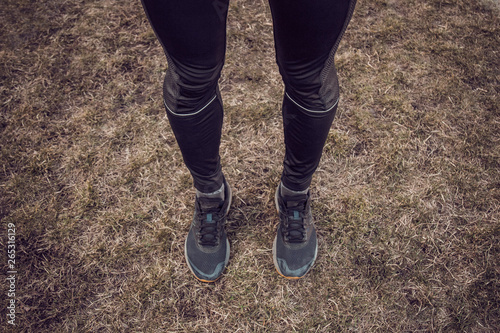 runner's legs in black sports leggings and sneakers on green grass top view. copy space. training in open space, outdoor. training preparation