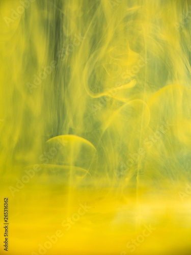Abstract acrylic smoke under water. Close up view. Blurred background. Selective soft focus. Dropplets of yellow ink dissolving into water, abstract pattern. Paint mixing with liquid