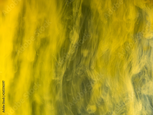 Flows of yellow acrylic paint under water, abstract background. Close up view. Blurred background. Abstract acrylic waves mixing with water, abstract pattern. Drops of ink dissolving into liquid