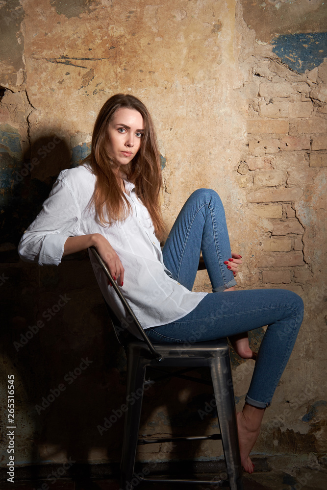 Young attractive girl or model wearing a white shirt siting on the chair.