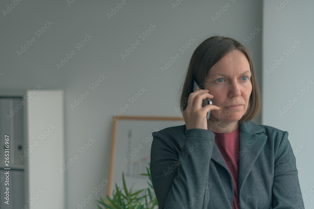 Serious businesswoman talking on mobile phone in office Serious businesswoman talking on mobile phone in office