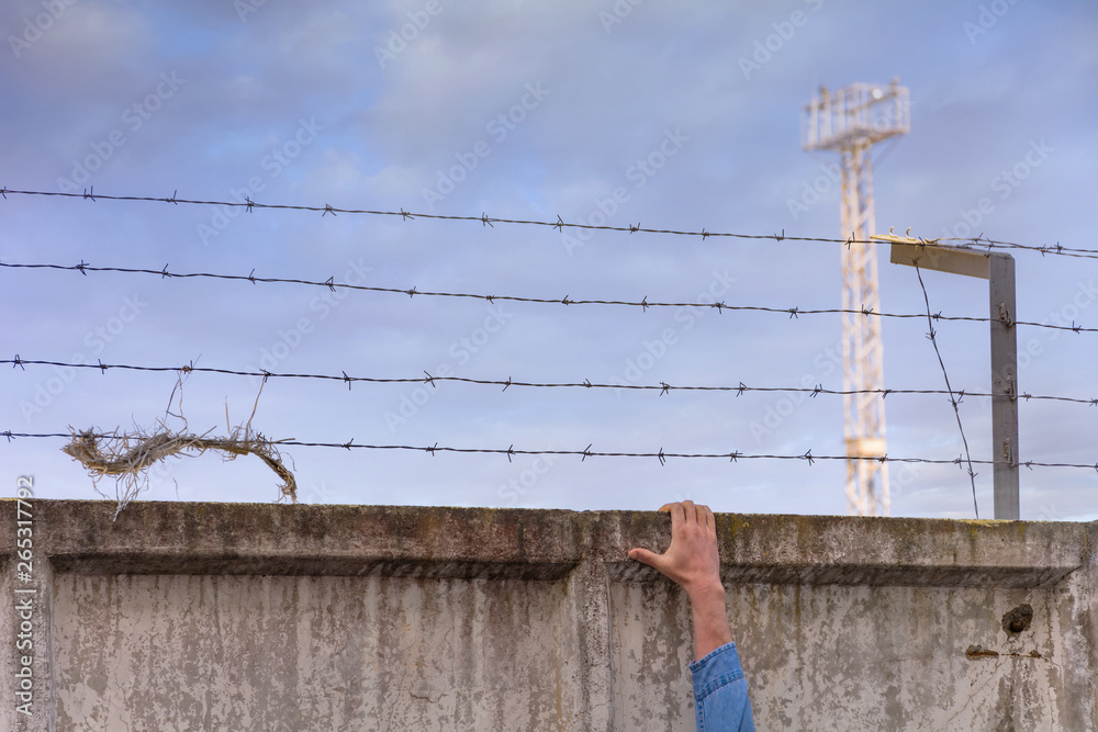 Fototapeta premium Escape from jail. Prison wall with barbed wire and a watchtower on blue sky background.