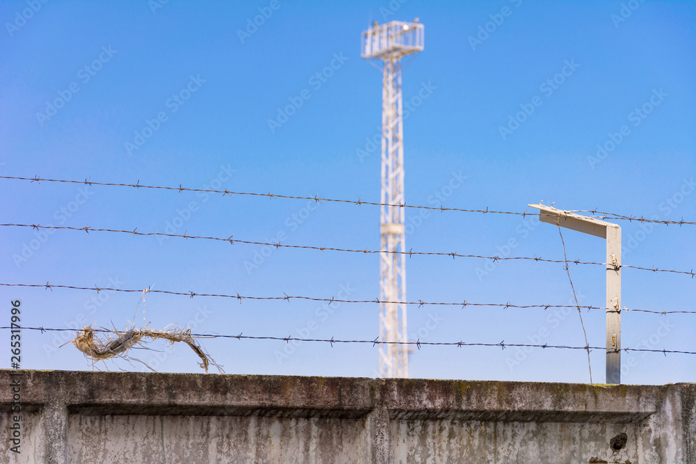 Concrete wall, against the backdrop of barbed wire, the concept of prison, salvation, refugee, lonely. Barbed wire fence detail.  Silhouette barbed wire and a watchtower