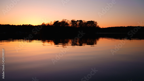 Romantic sunset over the lake. The silhouette of the trees reflects in the calm waters. Colorful landscape background, atmospheric and tranquil. 