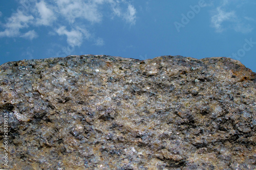 Rock or stone on blue sky with clouds background. Granite crouan rim or pick edge like cliff or mountain. Geology mineral texture closeup on two thirds photo