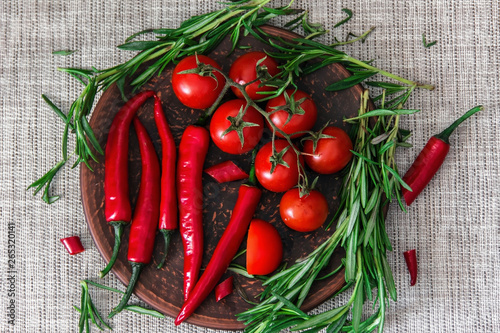 Fototapeta Naklejka Na Ścianę i Meble -  Fresh cherry tomatoes, sprigs of rosemary and chili peppers on a clay plate on the table. Fresh vegetables, herbs and spices - the concept of healthy eating. Food Photography - Image