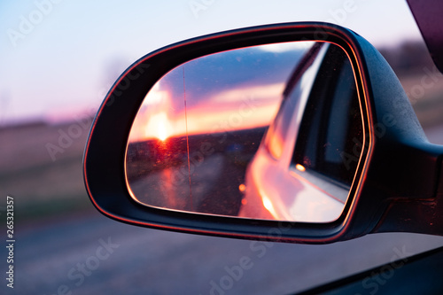 The reflection of the setting sun in the rearview mirror of the car