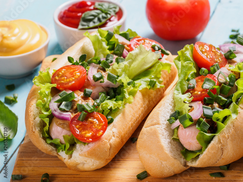 Close up view of homemade hotdogs with chicken, sausages, fresh vegetables, ketchup and mustard sauce on blue wooden background. Hot-dogs with tomatoes, onion, basil, letucce and spices.