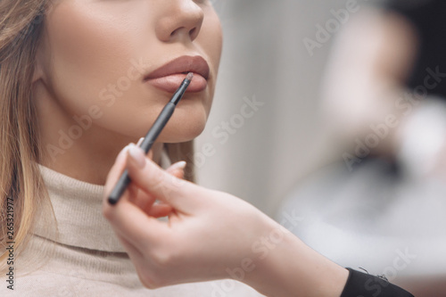 Young red-haired woman make-up artist puts make-up on the face of a beautiful blonde girl in a beauty salon. Concept of personal care and celebration preparation