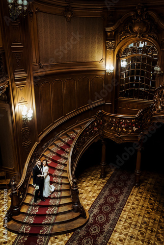 stylish luxury bride and handsome elegant groom on old wooden stairs on the background of luxury interior