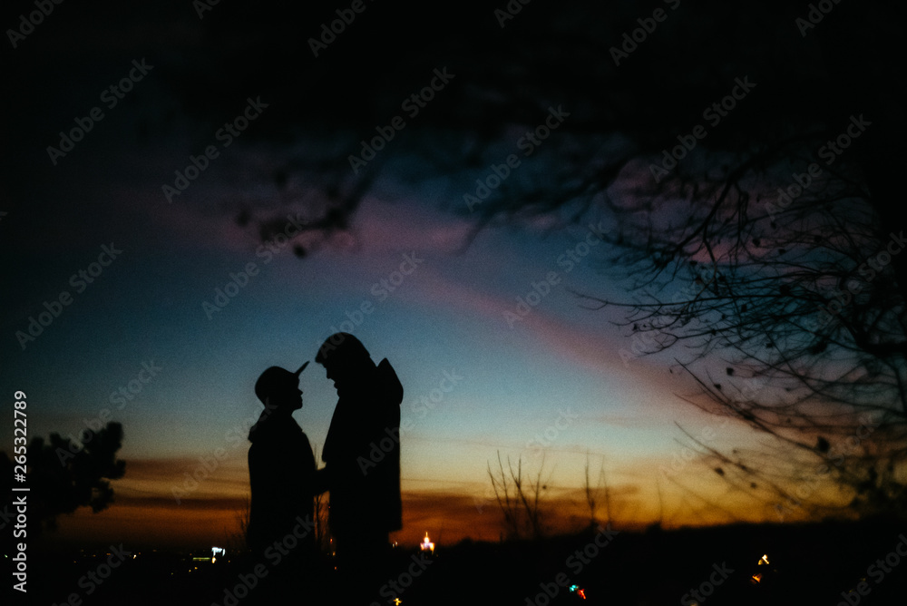 Fototapeta premium silhouette of happy couple looking at each other and touching with gentle on background of sunset sky and city lights
