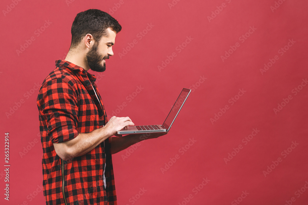 Picture of handsome man in casual t-shirt holding laptop and chatting or working isolated over red background. Picture of handsome man in casual t-shirt holding laptop and chatting or working isolated over red background.