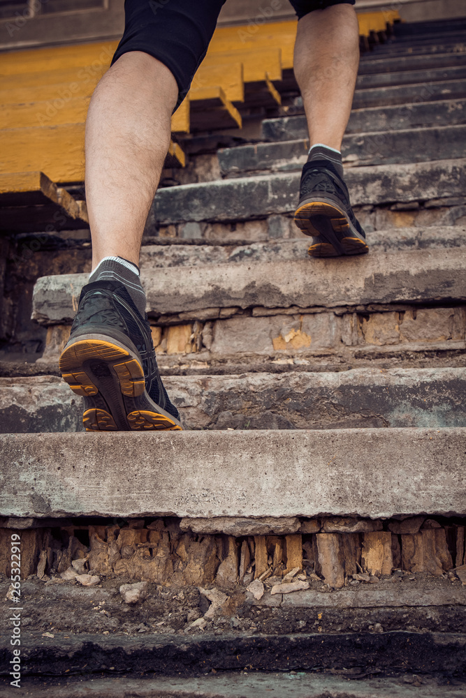 man trains in running on the stairs. Track and field runner in sport uniform training outdoor. athlete, below view. step exercises. vertical. pumped up shanks close up man trains in running on the stairs. Track and field runner in sport uniform training outdoor. athlete, below view. step exercises. vertical. pumped up shanks close up