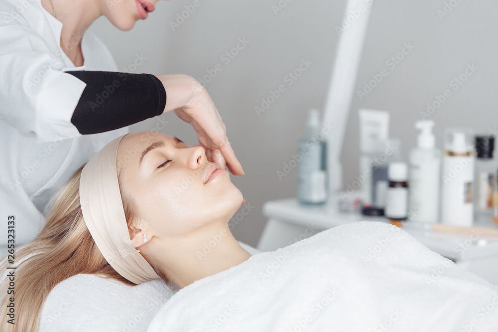 Unknown masseuse beautician doing a face massage to her client a beautiful young woman. Skin care concept
