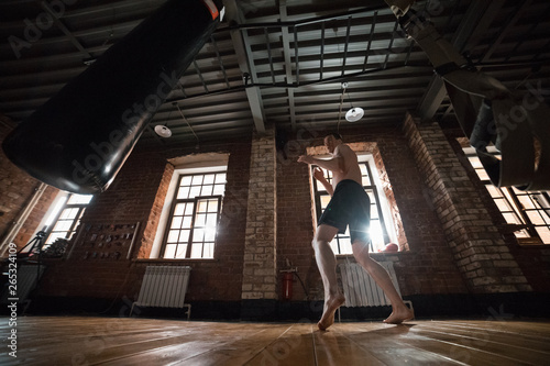 An athletic man boxer training with a punching bag in the gym