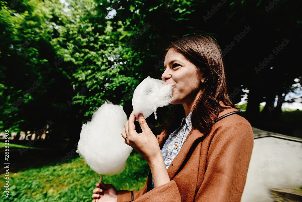 happy stylish girl holding big cotton candy and eating in amusement park in sunny spring time happy stylish girl holding big cotton candy and eating in amusement park in sunny spring time
