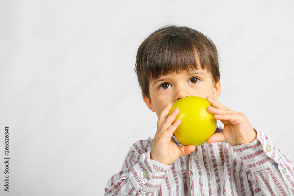 Small caucasian boy with dark hair, big dark eyes, wearing striped shirt is eating, biting big green apple, isolated on white background Small caucasian boy with dark hair, big dark eyes, wearing striped shirt is eating, biting big green apple, isolated on white background