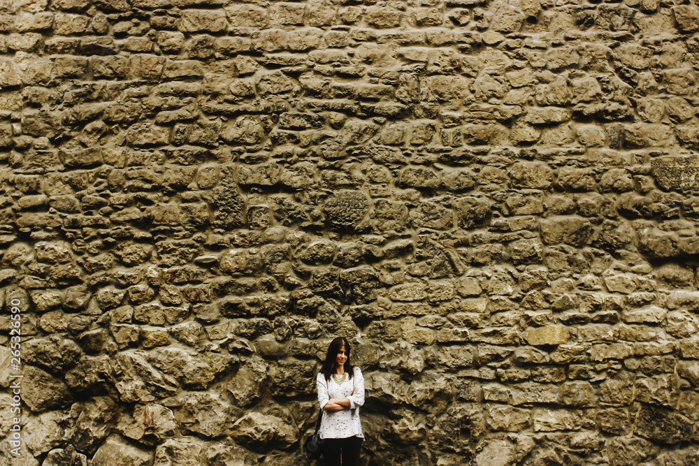 Φωτογραφία beautiful woman hipster standing at big old brick wall and smiling, traveling in