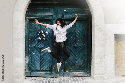 happy stylish hipster woman jumping and having fun on background of old wooden door at european street