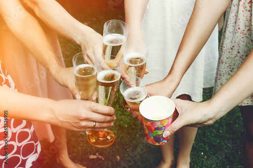 hands of woman holding colorful glasses and toasting champagne at joyful party in summer park, bridal shower or wedding reception