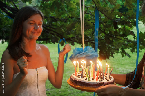 happy woman making a wish and blowing candles on cake at her bridal shower in summer park, joyful moment at party or birthday