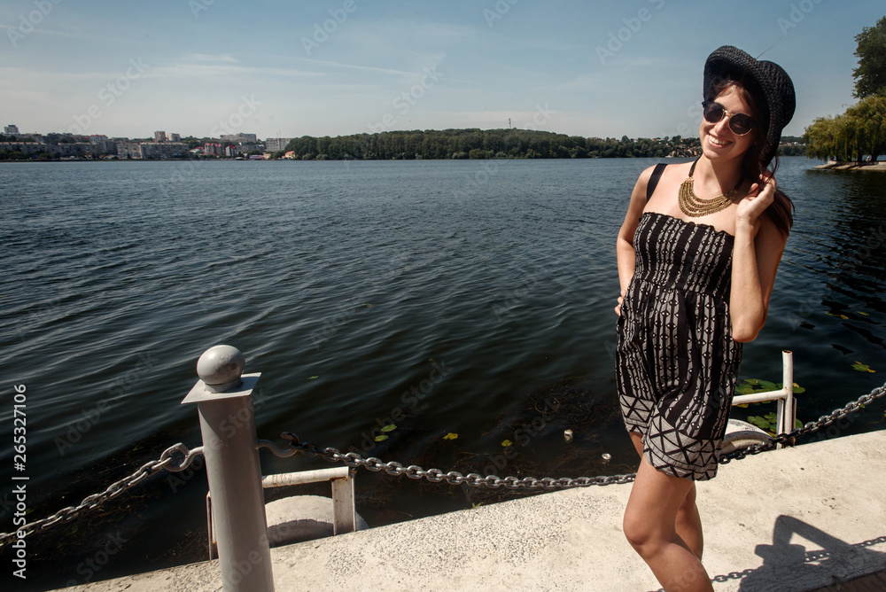happy stylish woman hipster holding hat and smiling at sunny shore, summer travel concept, space for text