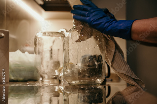 Hands in blue rubber gloves wipe glass jar